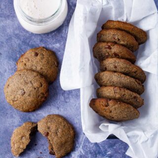 A basket filled with buttery buckwheat cookies, next to a cup of milk and some cookies spread out on the table.