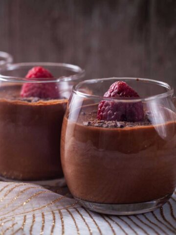 Mini glasses filled with chocolate mousse and topped with a fresh raspberry and shaved chocolate pieces.