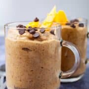 Two creamy mango smoothies topped with chocolate chips and fresh mango slices.