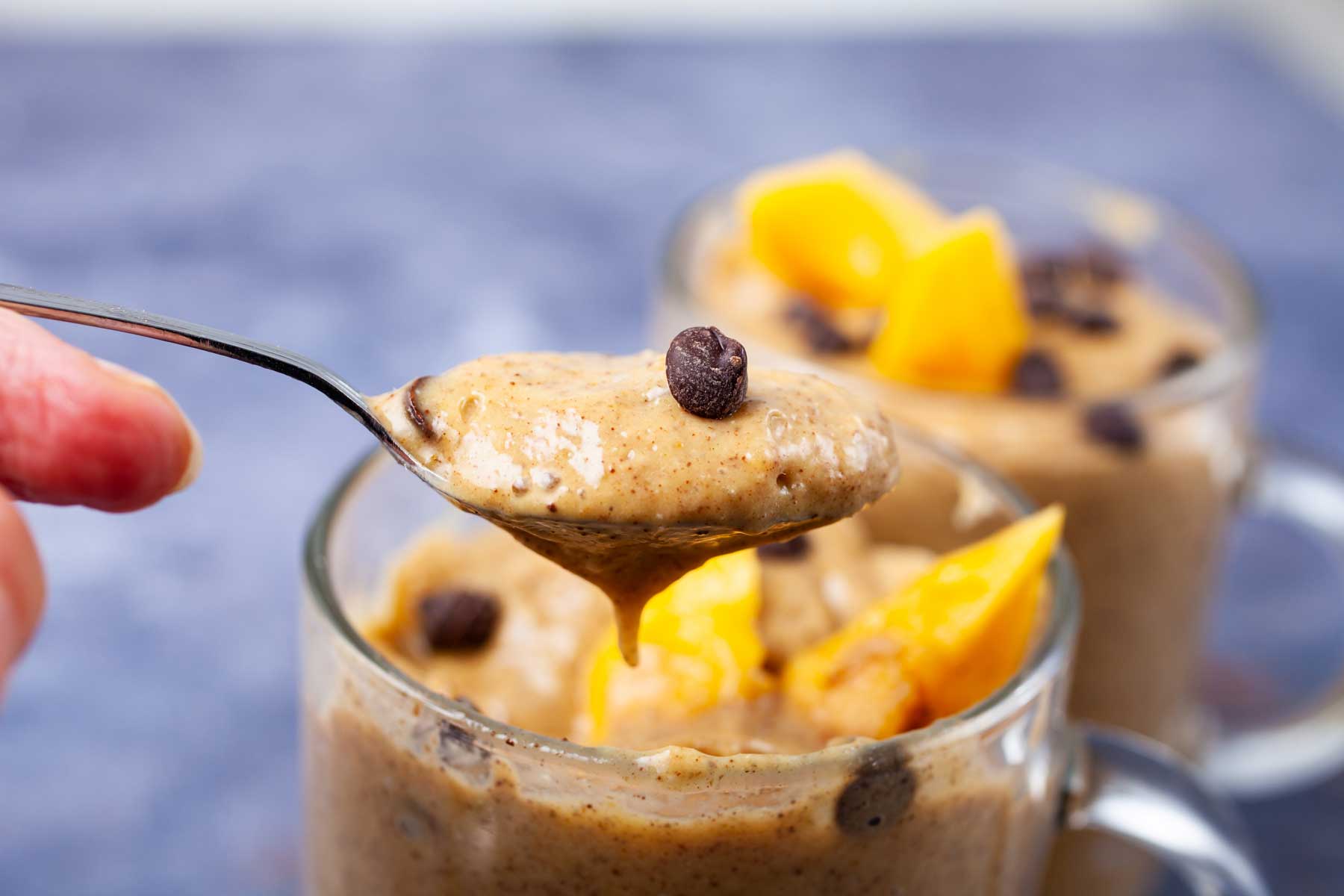 A spoon full of mango smoothie held on top of a smoothie filled glass.