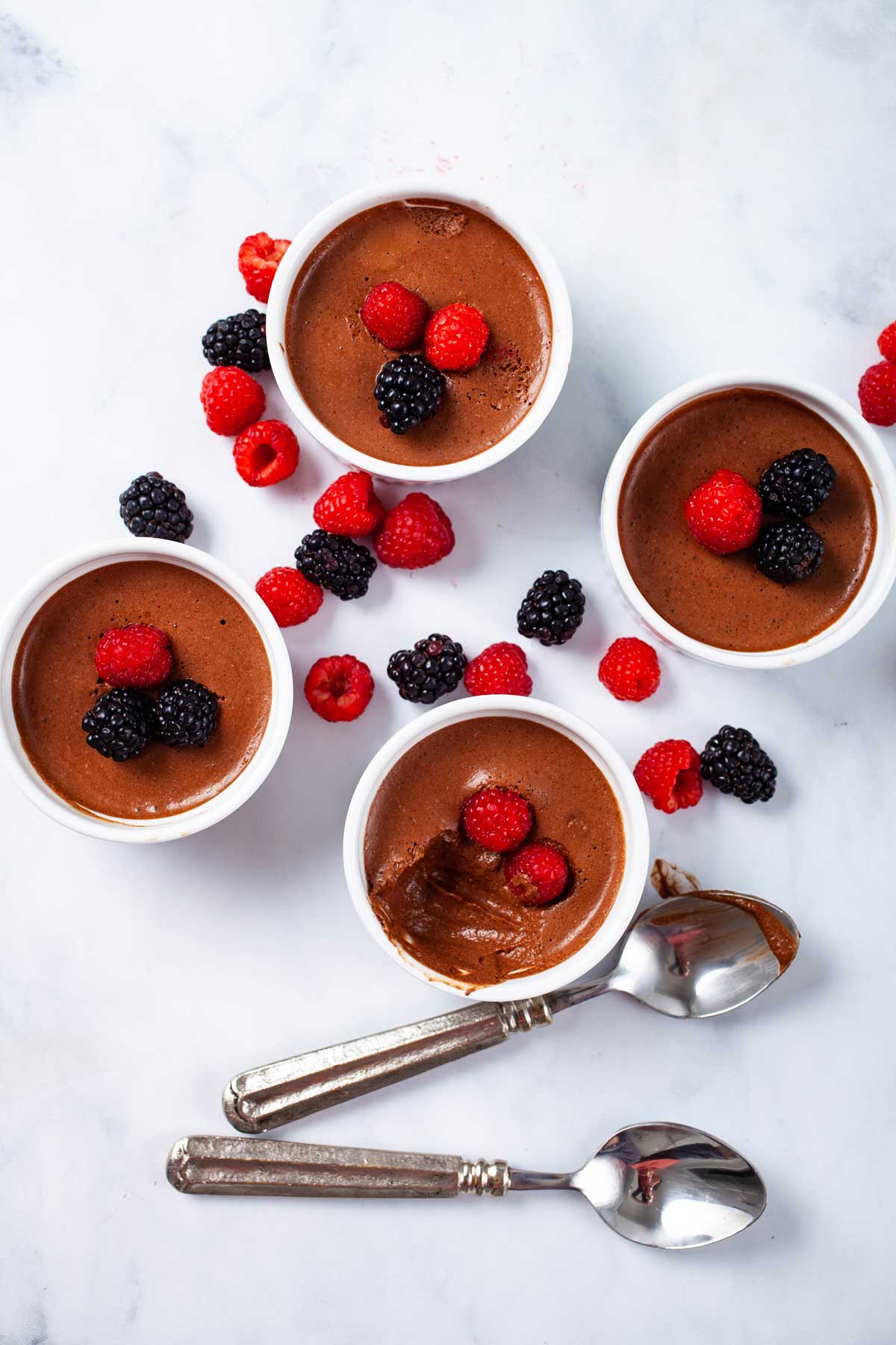 Four ramekins filled with chocolate mousse and topped with fresh berries.