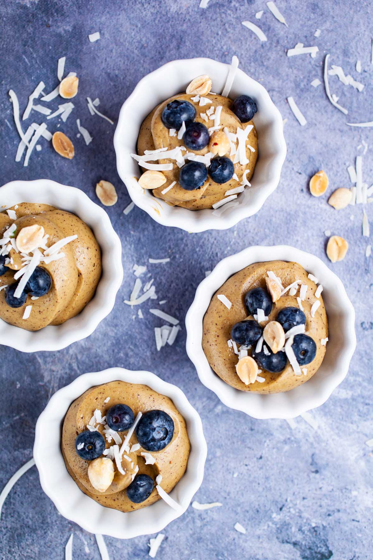 Small cups filled with vegan avocado mousse and topped with berries and coconut shreds.