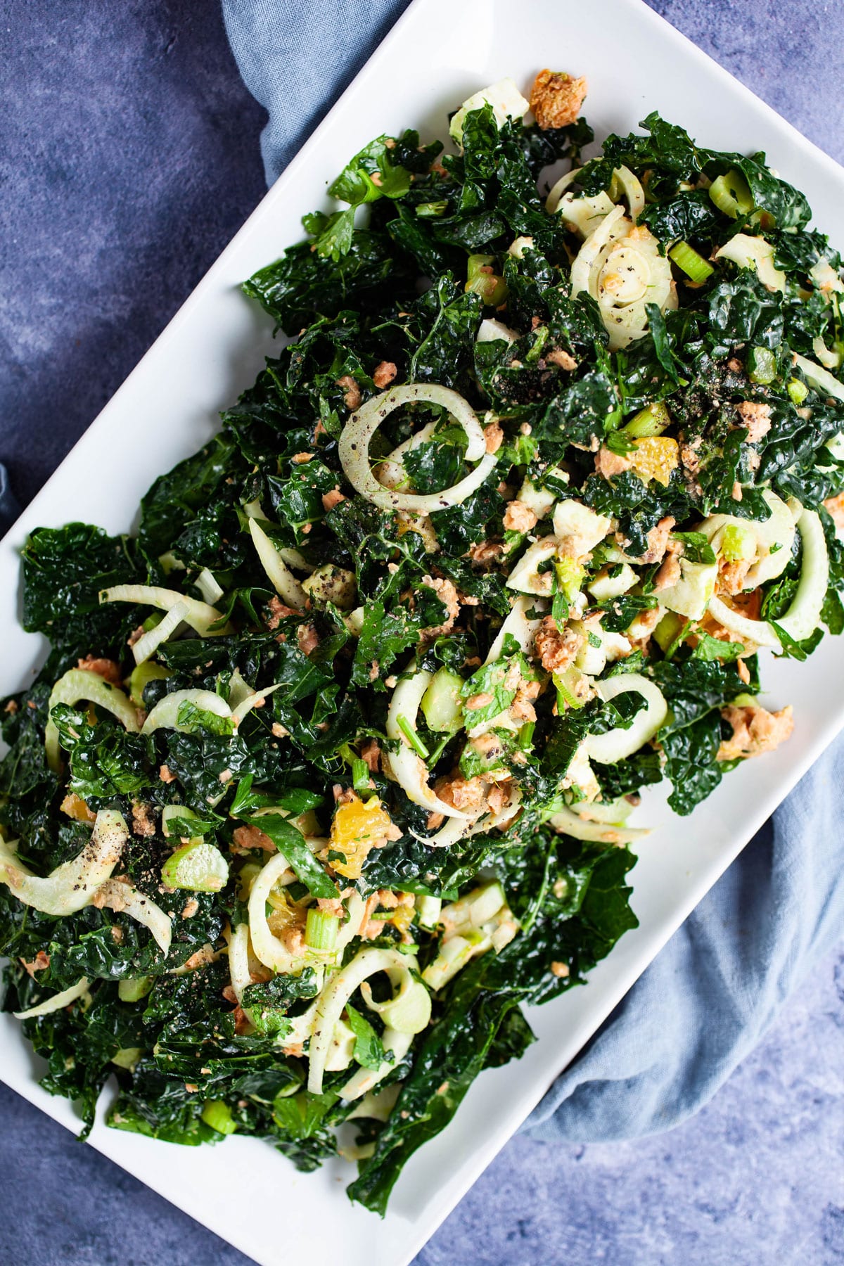 Chopped kale salad combined with sliced fennel, chopped oranges, chopped parsley leaves, salmon, and mozzarella cheese in a dijon mustard dressing on a serving plate.