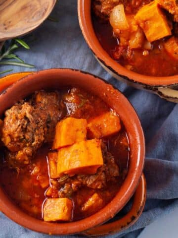 Two terracotta bowls filled with a meat sweet potato and stew.