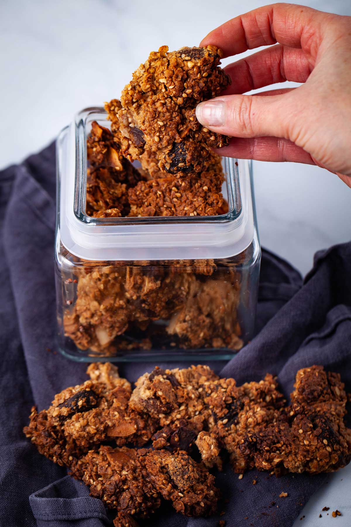 A hand holding a brown baked cluster of granola.