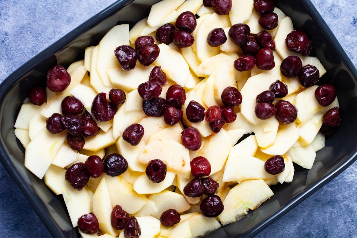 Sliced apples and cherries arranged in a baking pan.