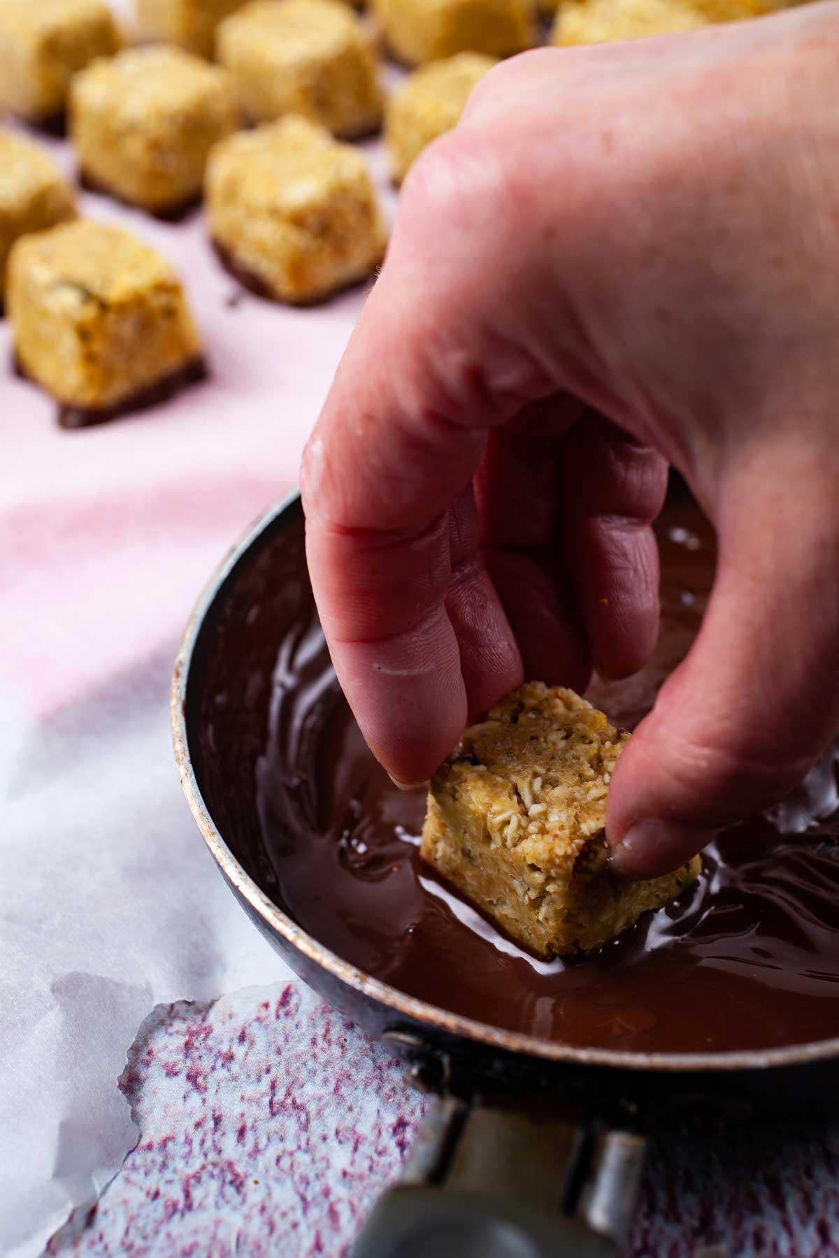 A hand dipping a coconut bite into melted chocolate.