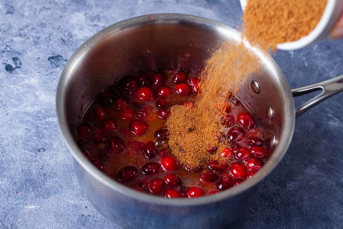 Coconut sugar added to a small pot filled with fresh cranberries.