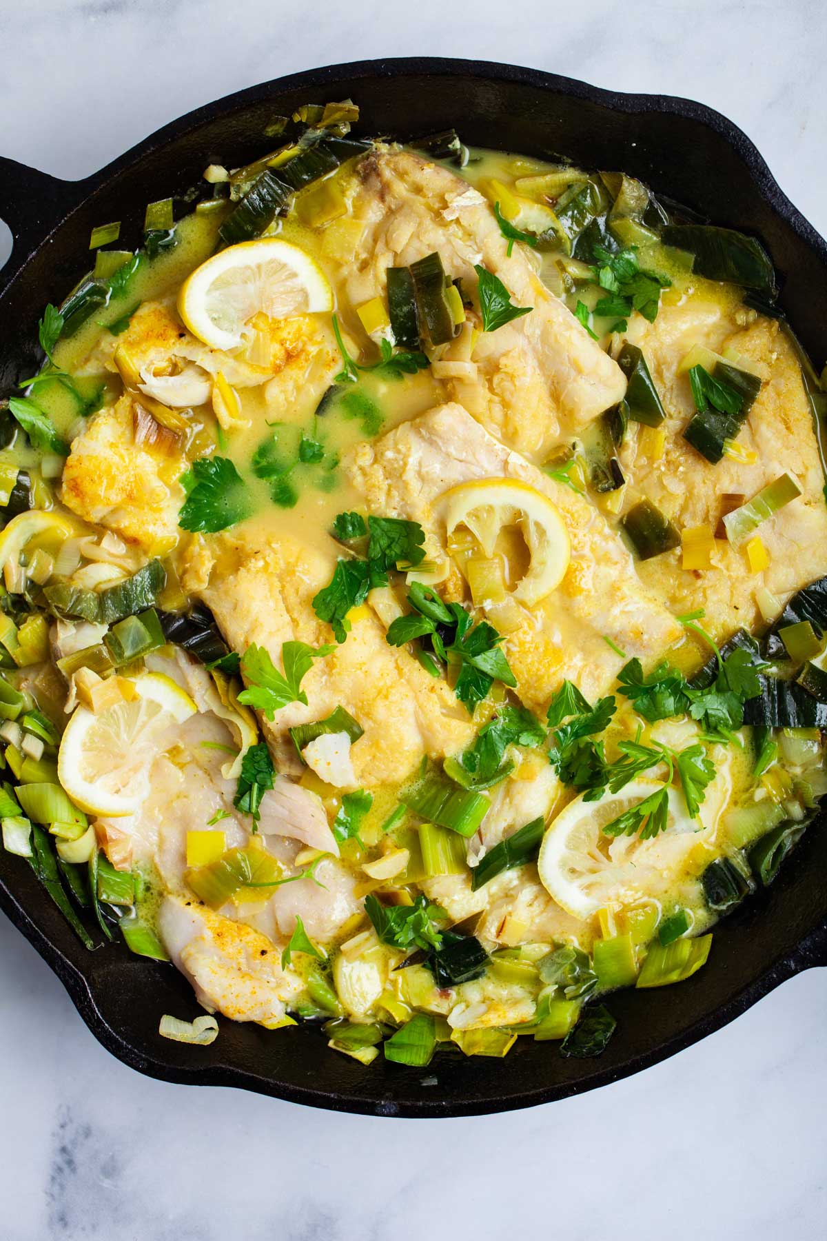 Creamy cooked cod and leek in a cast iron pan.