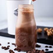 A hand stirring in a cold brew smoothie in a small glass jar.