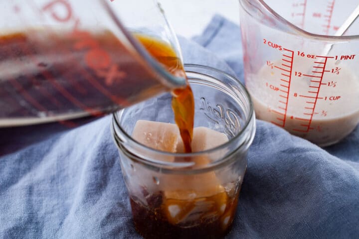 Coffee being poured into a mason jar with cashew milk ice cubes.