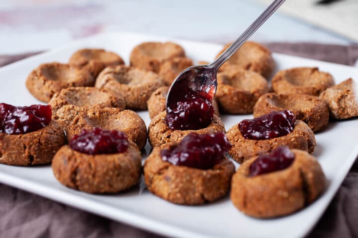 Someone spooning jam in thumbprint cookies.