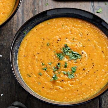 Creamy carrot soup served in a black bowl.