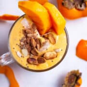 A persimmon smoothie topped with cinnamon, nuts, and garnished with fresh persimmon slices.