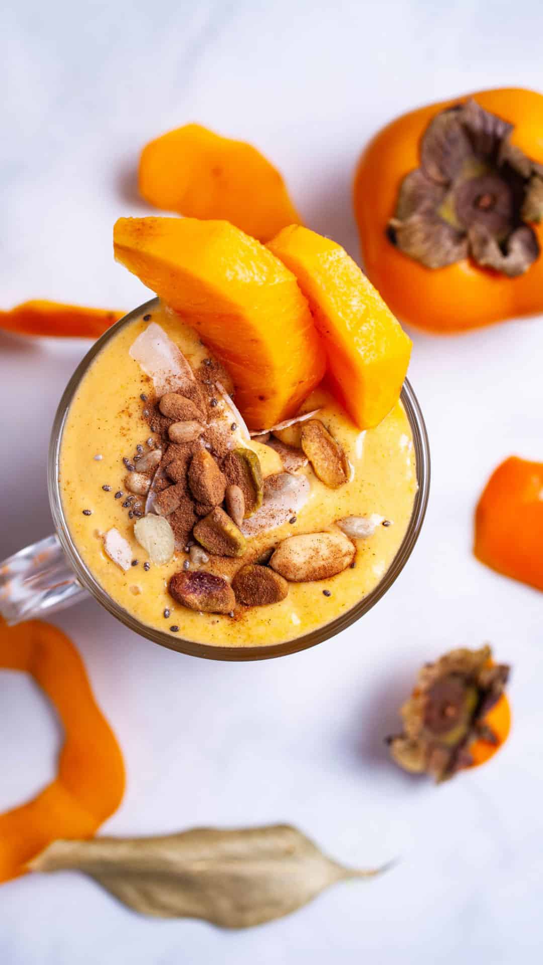 A persimmon smoothie topped with cinnamon, nuts, and garnished with fresh persimmon slices.