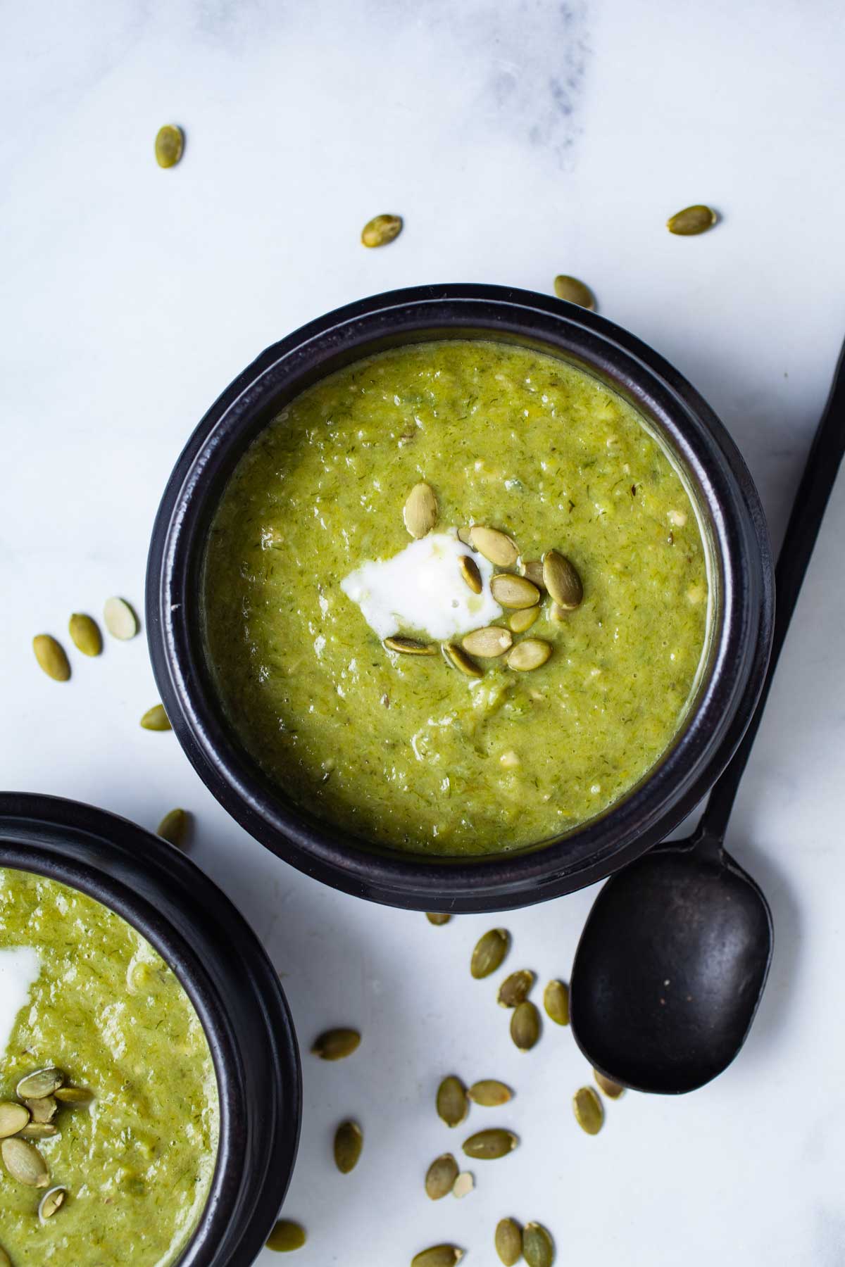 Avocado leek soup served in small bowls topped with seeds and coconut cream.