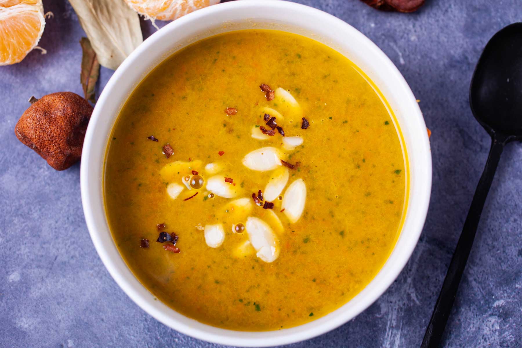 Orange soup in a white bowl topped with shaved almonds and chili flakes.