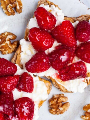 Two toasts on a plate with peanut butter, cottage cheese, fresh berries and a drizzle of honey.