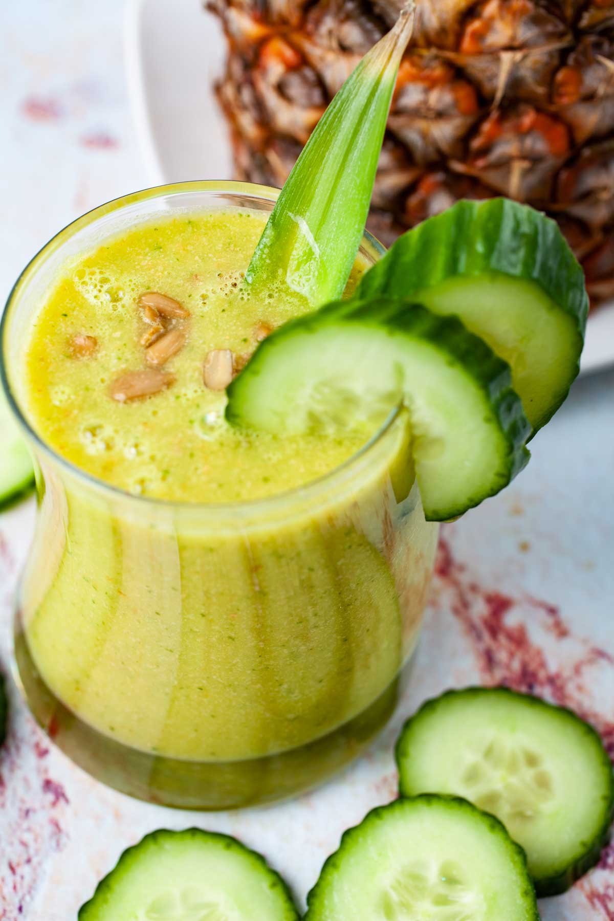 Creamy pineapple cucumber smoothie topped with seeds and garnished with extra cucumber slices.