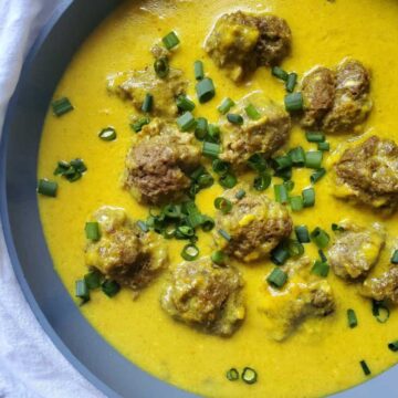 Mini meatballs dunked in a curry sauce and topped with green onions.