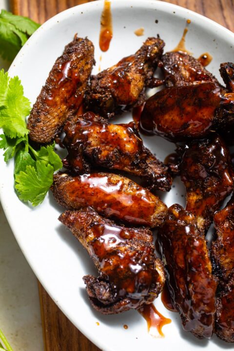 jerk chicken wings with guava sauce on a white platter.