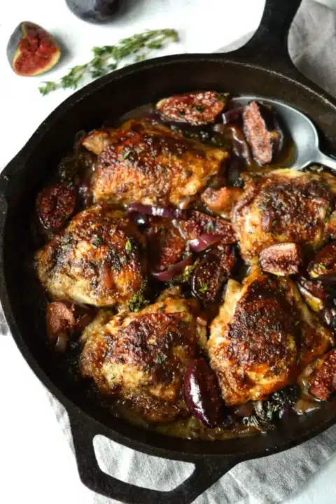 an overhead shot of a cast iron skillet filled with nicely browned and caramelized chicken thighs with pieces of fig nestled around.