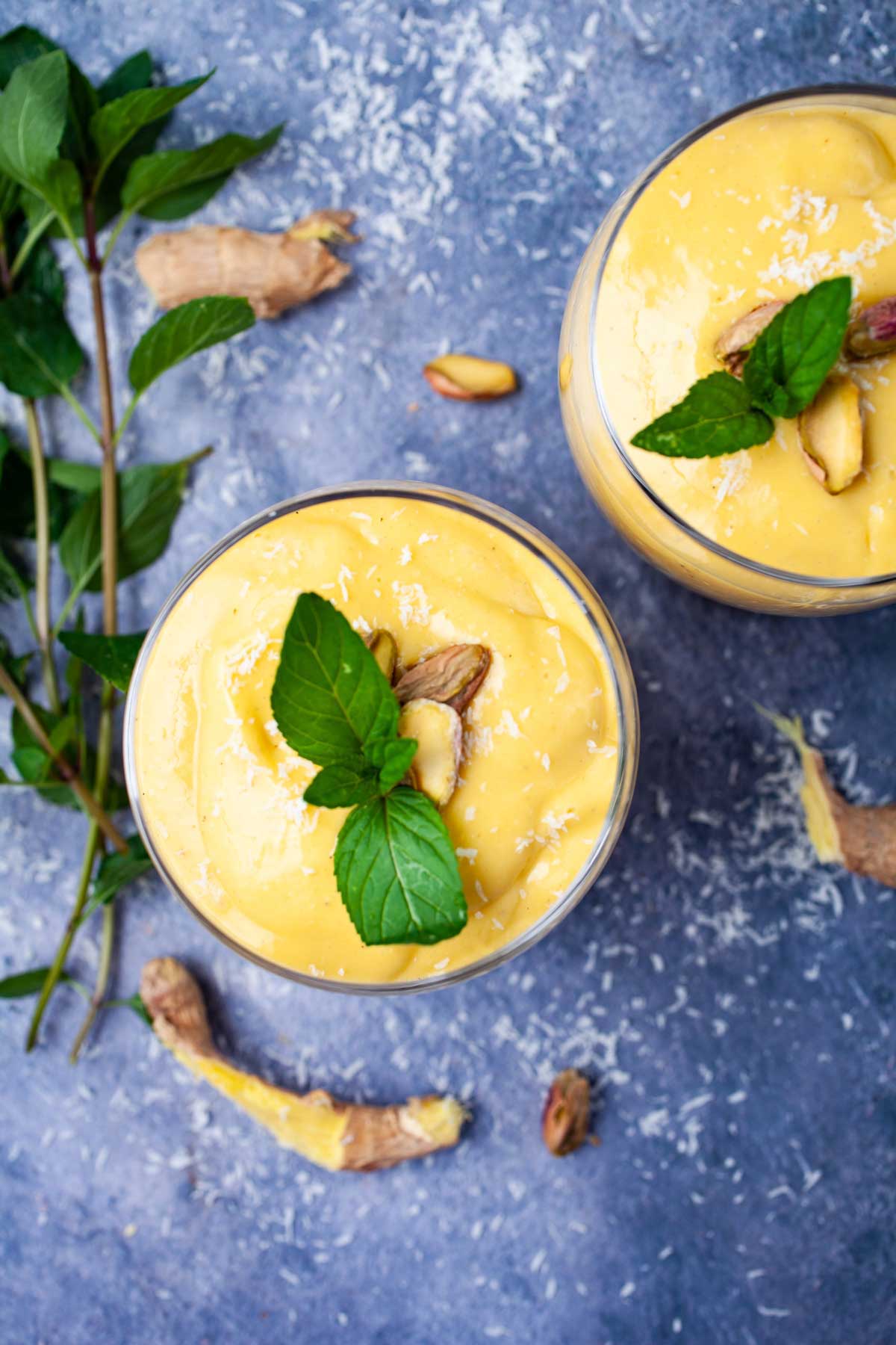 Glasses filled with dairy-free mango lassi and topped with fresh mint and pistachio nuts.