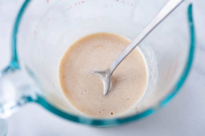 A teaspoon resting in a glass pyrex measurement cup with cashew milk.