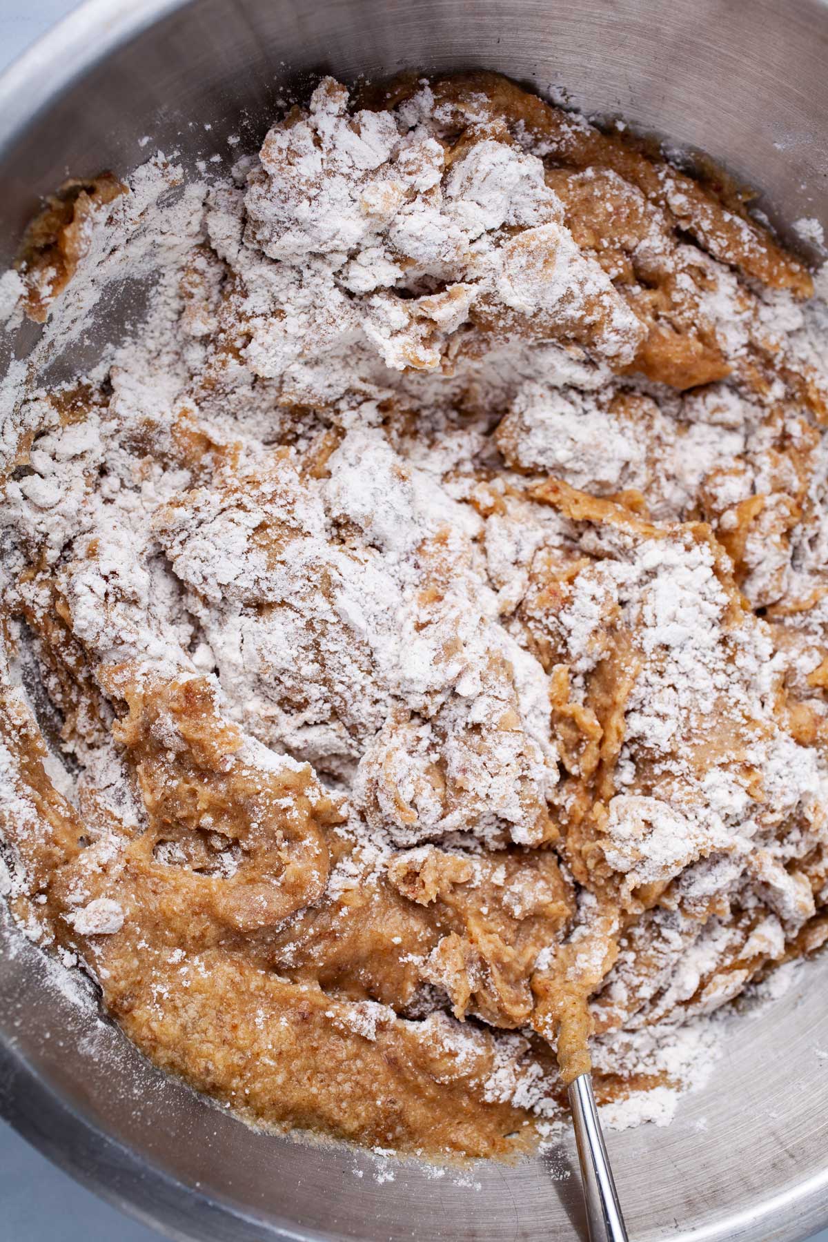 Flour is mixed with a brown paste in a stainless steel bowl.