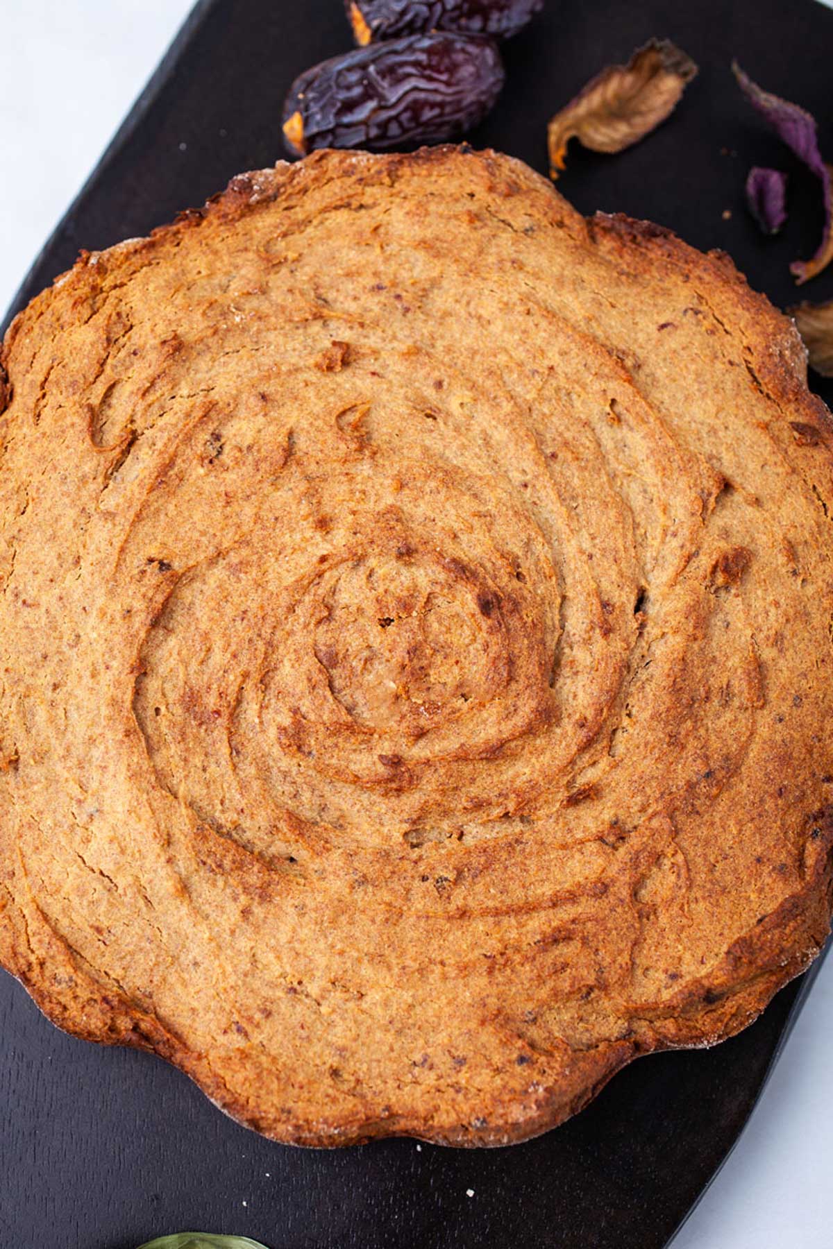 A brown baked date cake served on a wooden board.