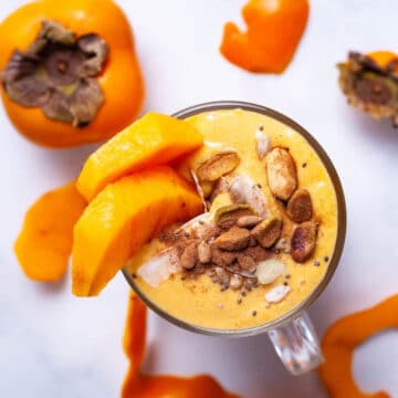 A persimmon smoothie topped with cinnamon, nuts, and garnished with fresh persimmon slices.