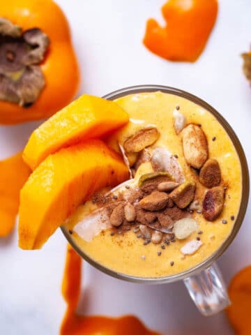 A persimmon smoothie topped with cinnamon, nuts, and garnished with fresh persimmon slices.