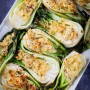 Baked baby bok choy topped with cheese served on a large white tray.