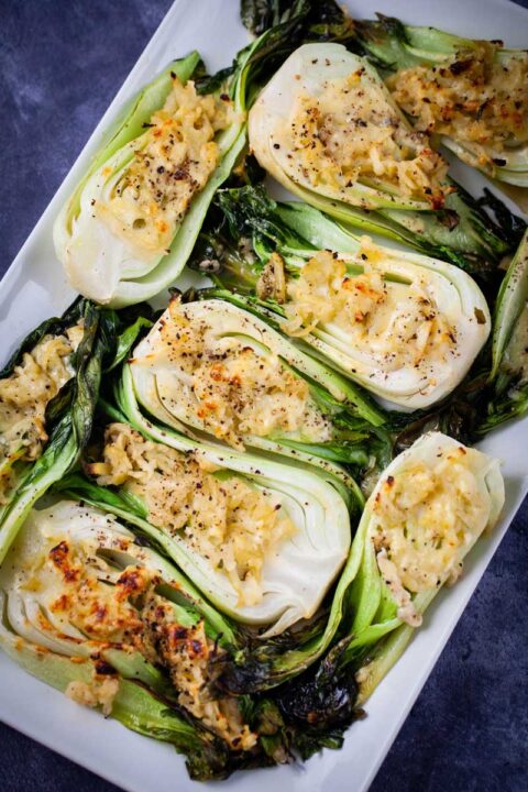 Baked baby bok choy topped with cheese served on a large white tray.