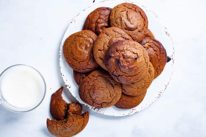 Soft baked golden brown peanut butter cookies stacked on a small plate next to a glass of milk and one crumbled cookie.