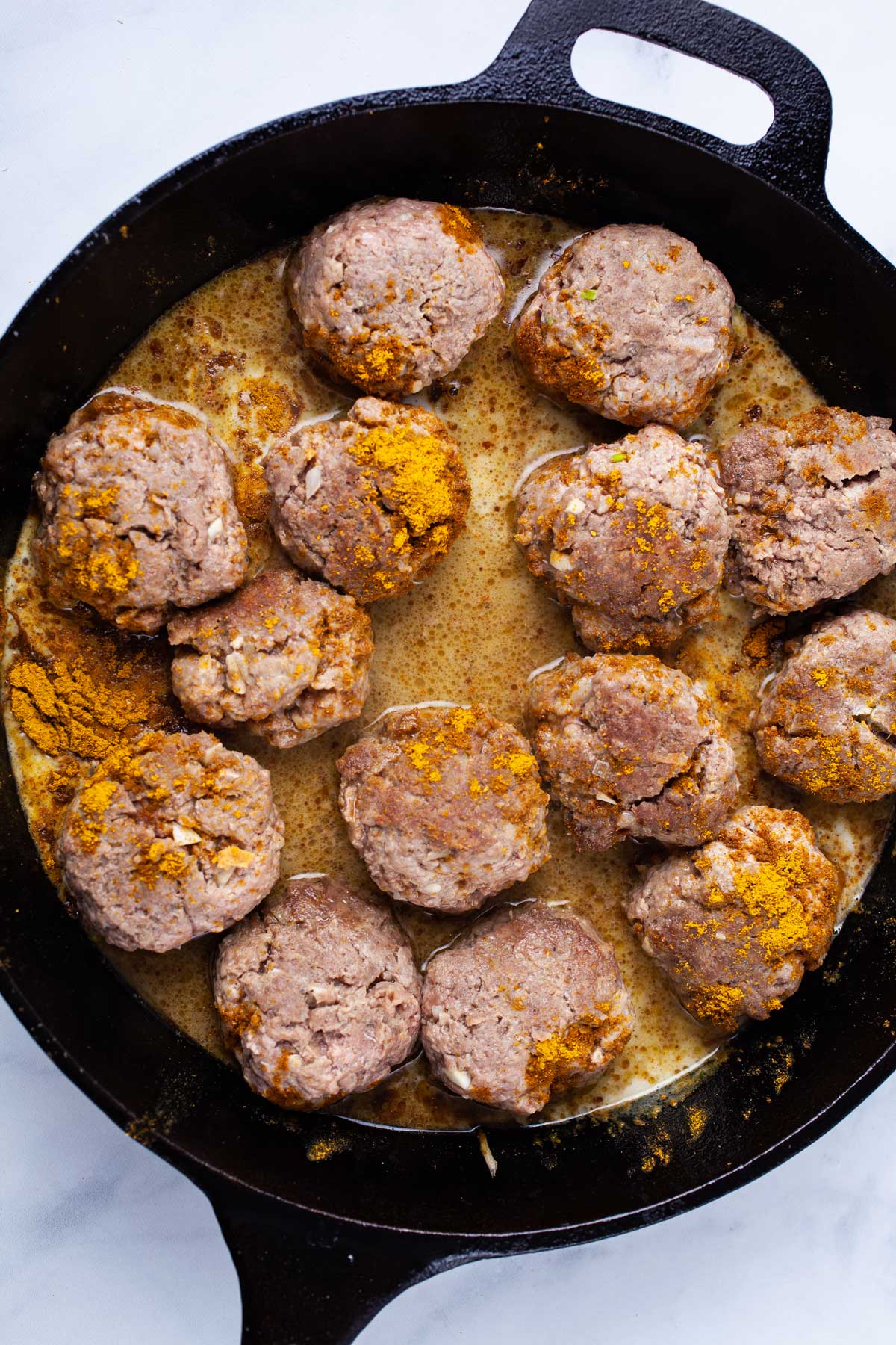 Seasoned meatballs in a cast iron skillet.