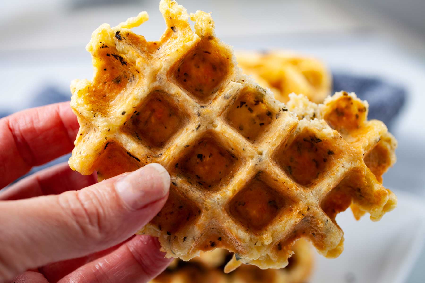 A hand holding a half eaten golden brown cheese waffle.