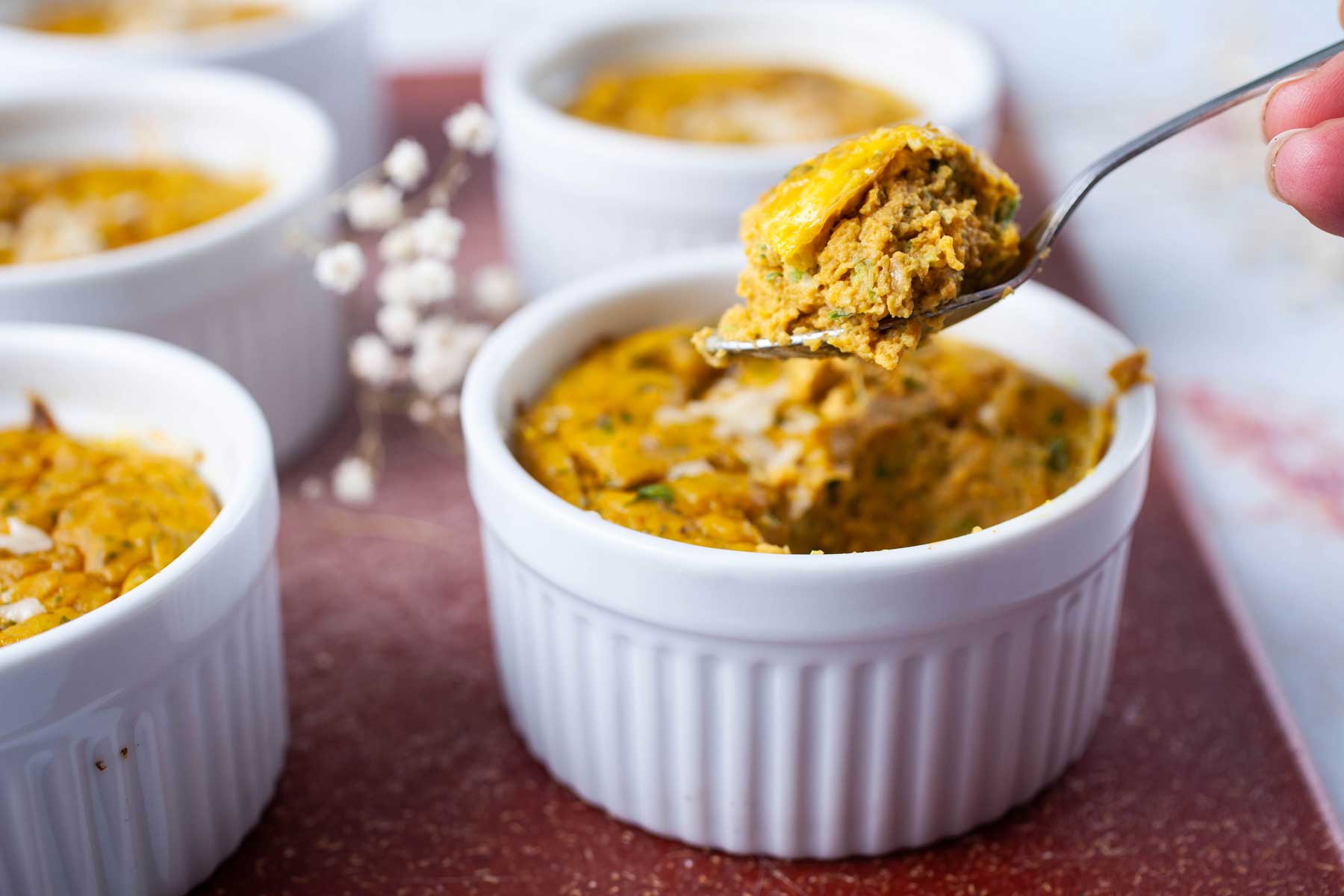 A spoon lifting a bite out of a mini frittata in a ramekin.