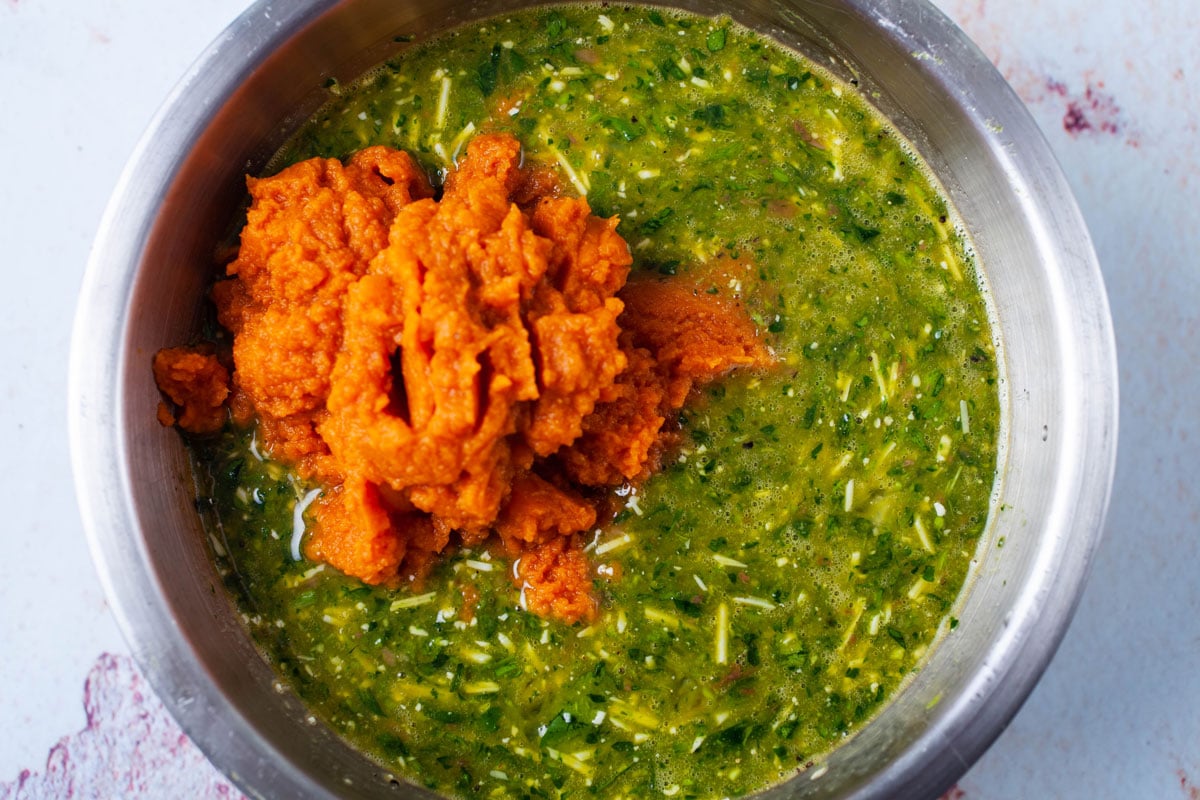 Mixed eggs, fresh parsley, cheese, and pumpkin puree in a bowl.