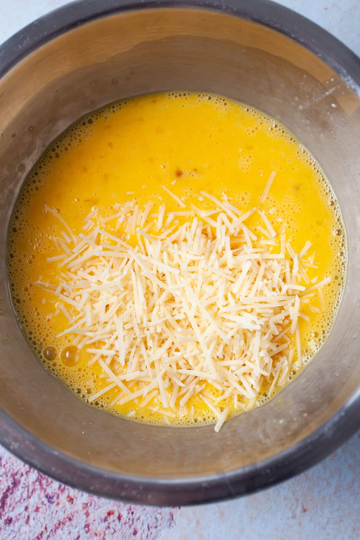 A bowl with blended eggs and grated cheese.
