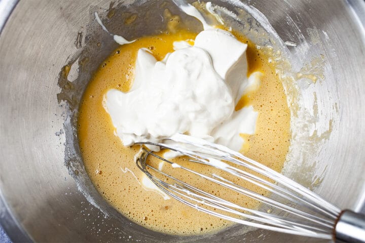 A whisk stirring whipped egg whites into wet ingredients in a stainless steel bowl.