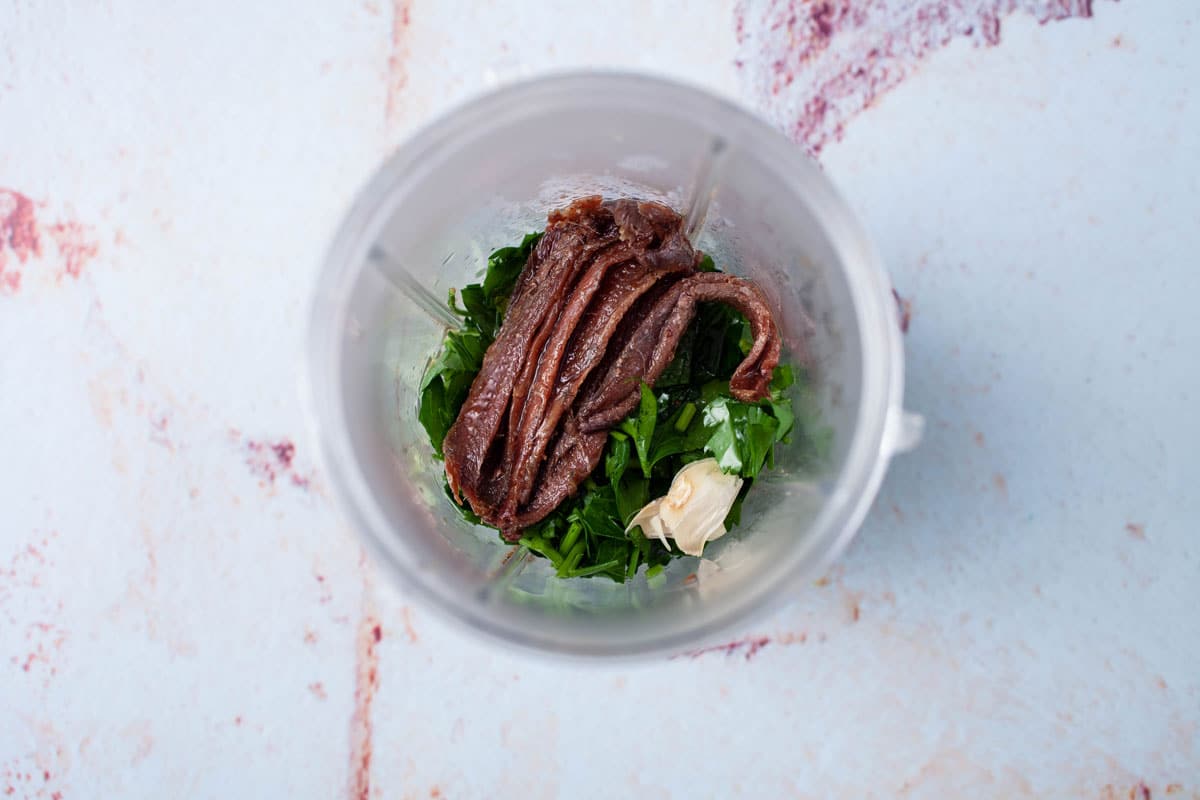 Fresh parsley, garlic cloves, and canned anchovies in a blender.