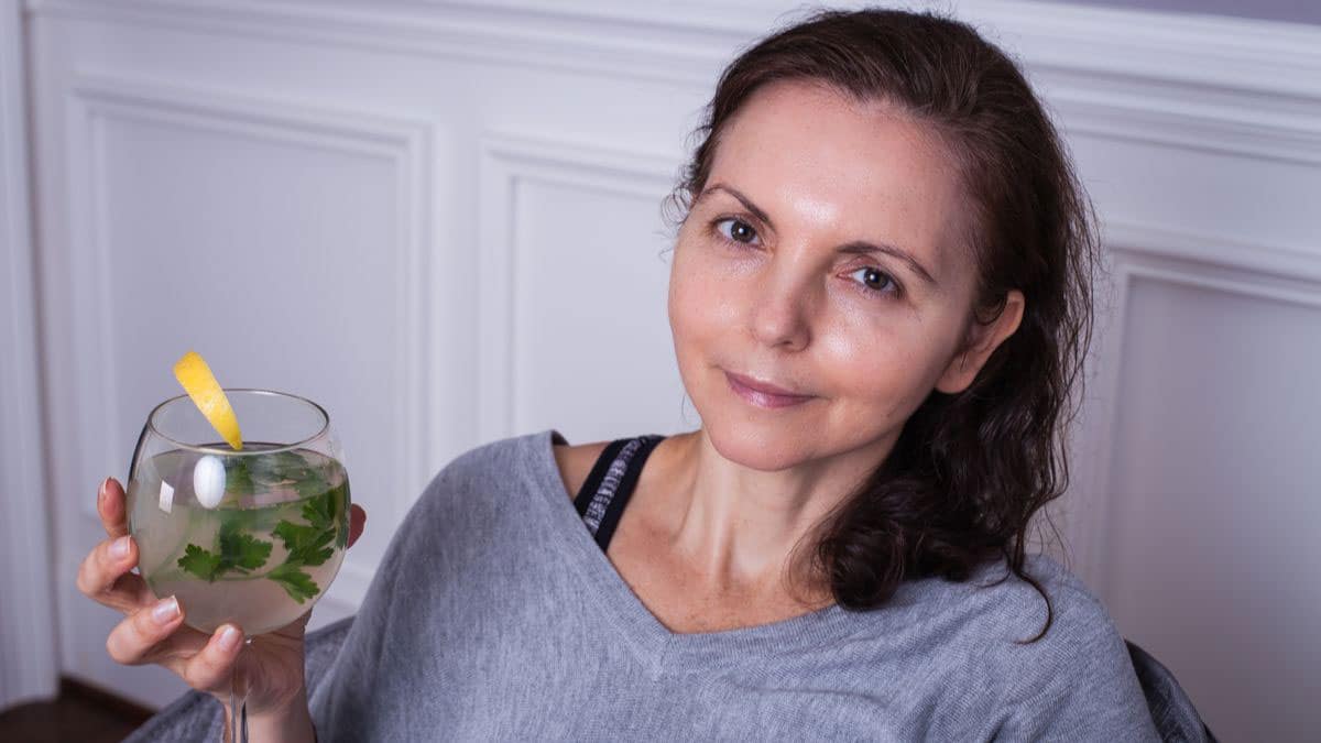 A smiling women holding a healthy mocktail in her hand.