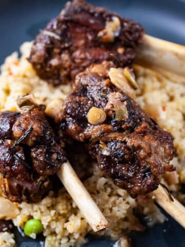 A plate containing cauliflower rice and topped with fall of the bone beef ribs.