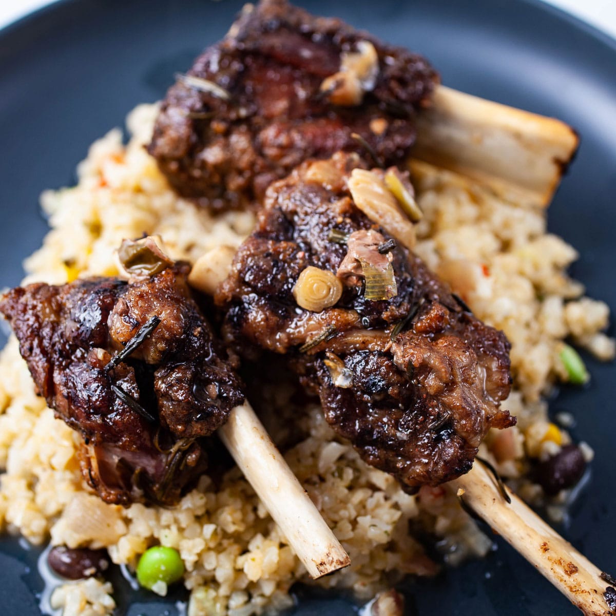 A plate containing cauliflower rice and topped with fall of the bone beef ribs.