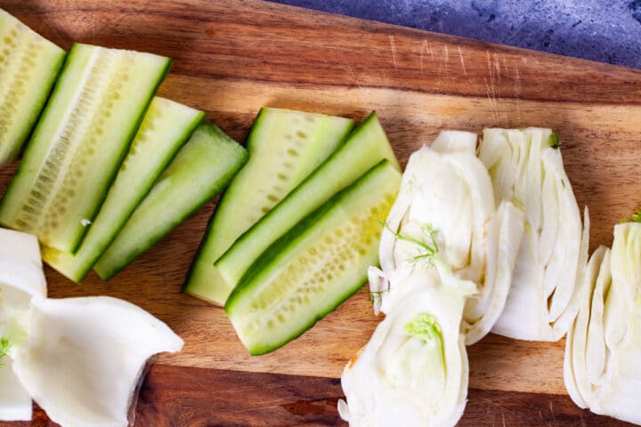 Fresh cucumber and fennel slices laid out on a wooden board.