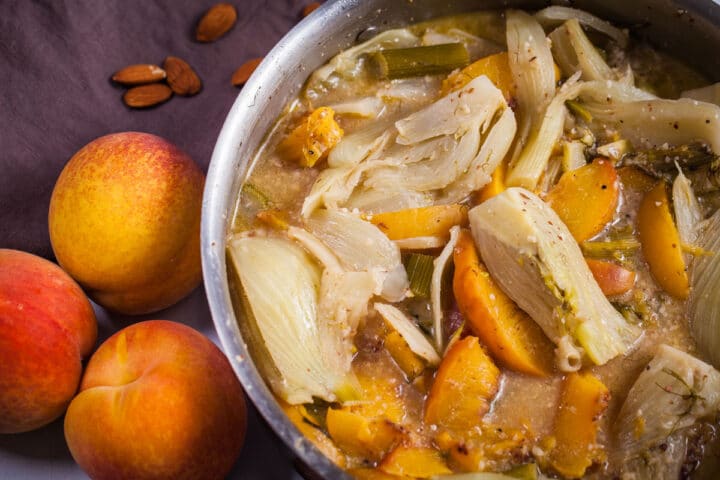 Soft braised fennel pieces and peaches in a creamy liquid in a large pan.