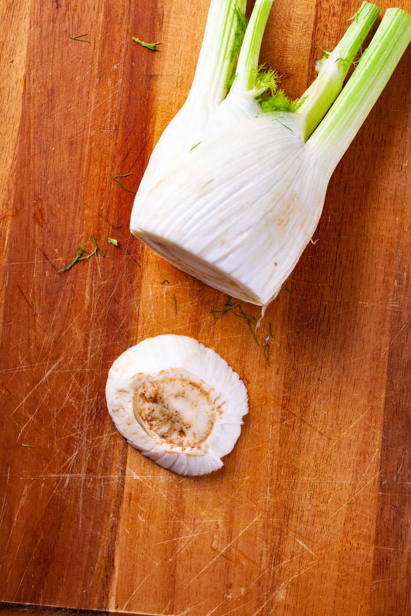 And end removed from a raw fennel bulb on a cutting board.