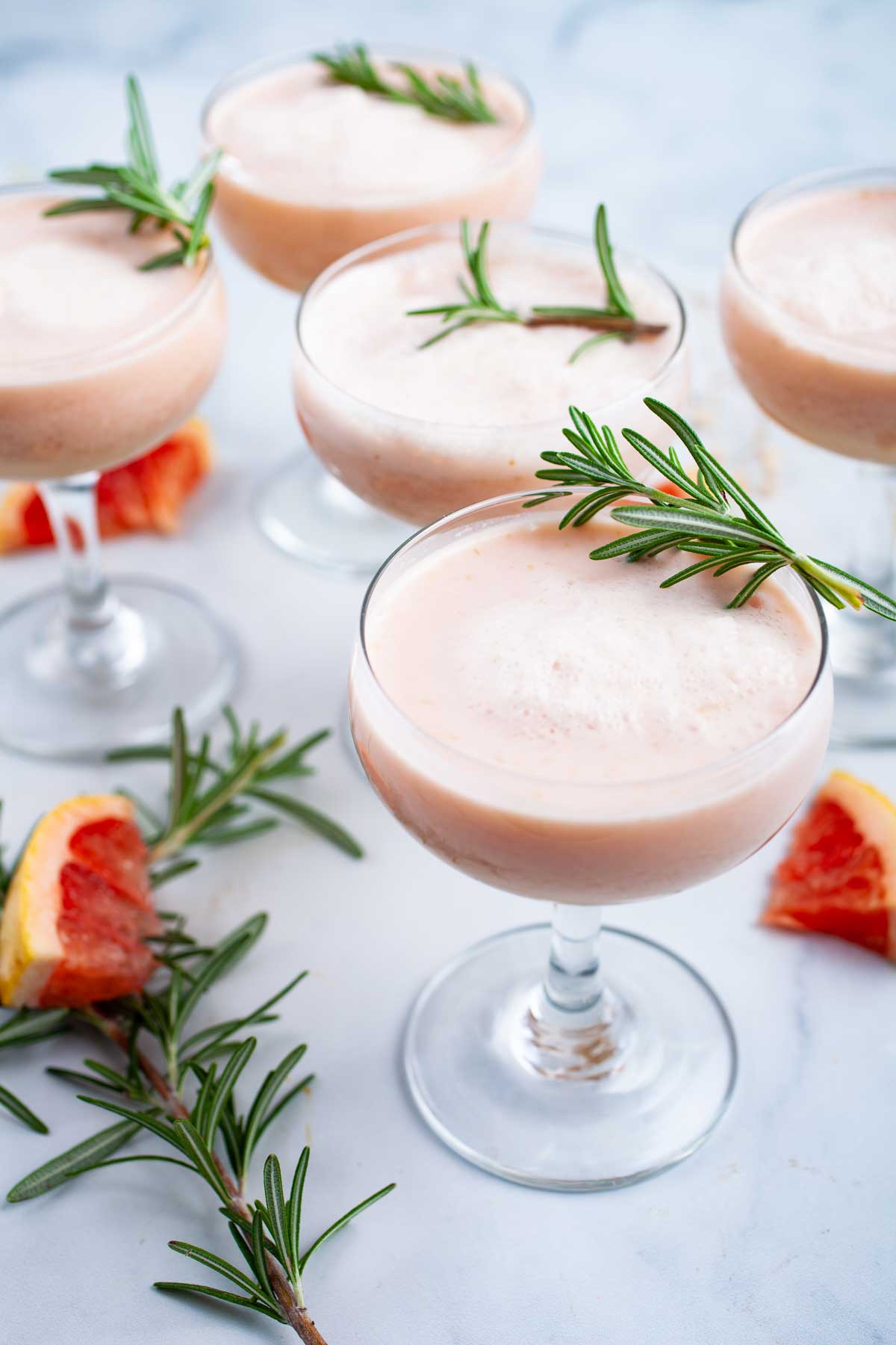 Grapefruit mocktails topped with Rosemary leaves served on a table.