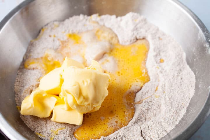 Butter, eggs, and yeast added to flour in a stainless steel bowl.